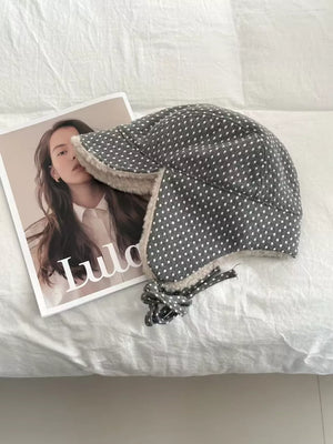 Gray polka dot fleece hat with cream lining and ear flaps tied with a bow.