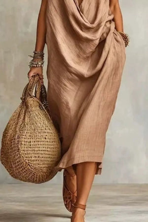 Tan midi dress with cowl neck and pockets, worn with sandals and a straw bag.
