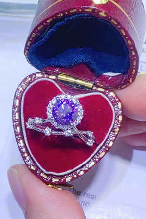Purple moissanite engagement ring set with halo and diamond accents in a heart-shaped box