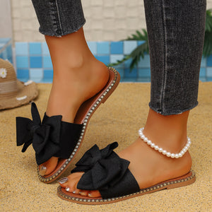 Black bowknot slide sandals with pearl anklet and frayed denim jeans.