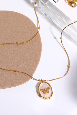Gold locket necklace with oval mother of pearl inlay and a detailed butterfly charm.
