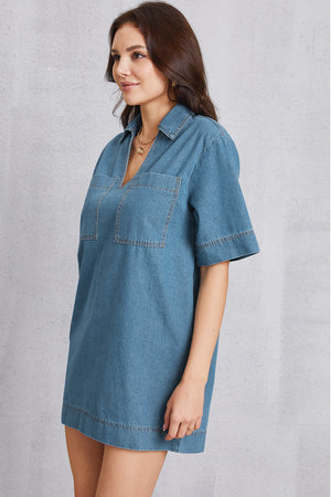 Denim mini dress in medium wash with plunging collar, short sleeves, and two chest pockets.