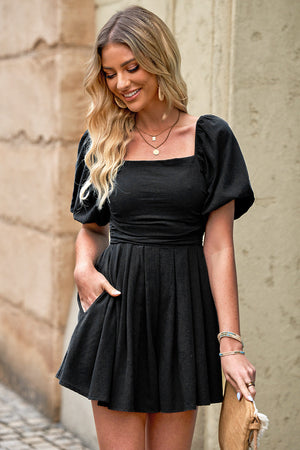 Black square neck puff sleeve romper with cinched waist and pleated skirt.