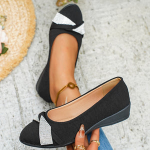 Black slip-on wedge flats with rhinestone bow detail.