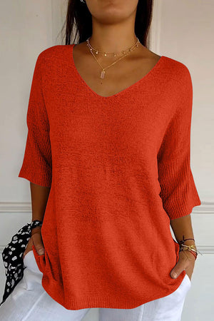 Red knit sweater with V-neck and flared sleeves, textured fabric.