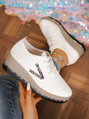 White wedge sneakers with colorful rhinestone embellishments on the side and sole.
