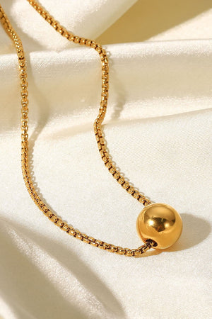 Gold orb pendant necklace with a box chain, on a satin background.