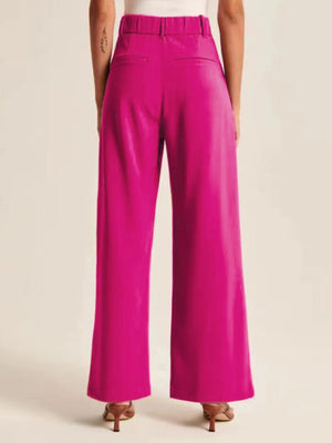 Magenta pleated palazzo trousers with a wide leg and elastic waistband, styled with heels.