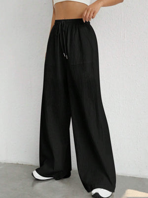 Black linen wide-leg drawstring trousers with pockets and a relaxed fit.