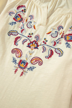 Pastel yellow blouse with colorful floral embroidery and V-neckline.