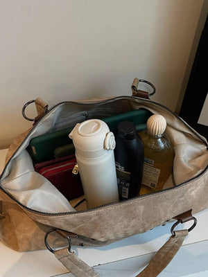 Distressed studded brown trapezoid bag interior view with water bottle, phone, and toiletries.