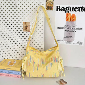 Yellow slouchy shoulder bag with colorful embroidered abstract pattern and side pockets.