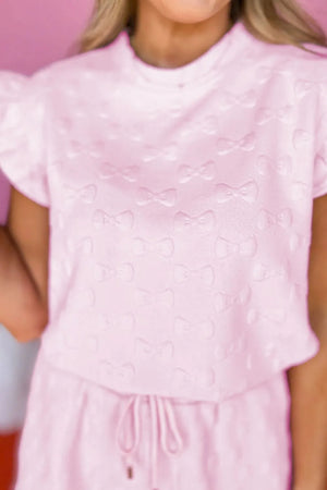 Blush pink loungewear set with embossed bows, ruffle sleeves, and drawstring waist.