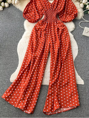 Scarlet polka dot smocked wide-leg romper with puff sleeves.