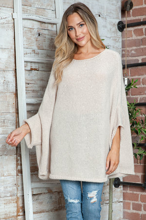 Cream knit sweater with cape sleeves and a relaxed fit, styled with distressed jeans.