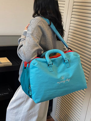 Blue duffel bag with embroidered sun and text, dual handles, and crossbody strap.
