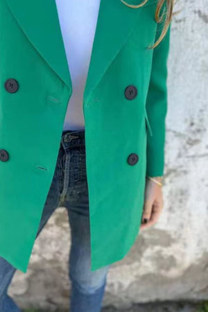 Green double-breasted blazer with sculpted lapels and dark buttons, styled with jeans.