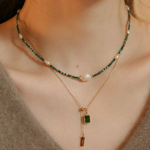 Layered necklace with green malachite beads, freshwater pearls, and a gold chain with emerald pendant.