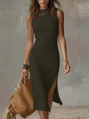 Sleeveless midi dress in sage with a high neckline and side slit, worn by a model holding a straw bag.