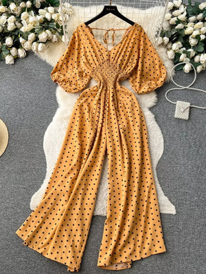 Yellow polka dot smocked wide-leg romper with V-neck and puff sleeves.