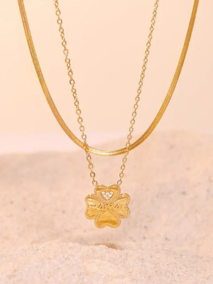 Gold layered necklace with a clover charm featuring a heart detail and small stones.