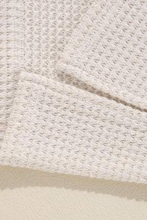 Beige waffle knit V-neck top with slit hem detail.