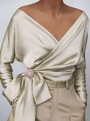 Draped satin blouse in cream with V-neck, brooch detail, and tie waist.