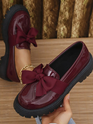 Burgundy patent platform loafers with large satin bows.