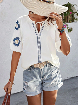 White embroidered yoke sleeve blouse with tie neck and blue floral details.