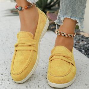 Yellow slip-on loafers with decorative knot detail and white soles.