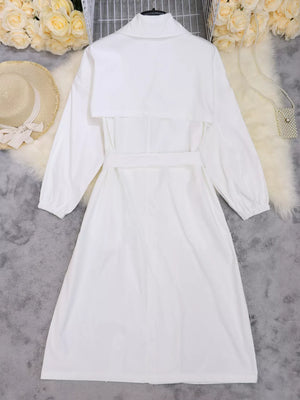 White midi dress with lapel collar, tie waist, and cuffed sleeves.