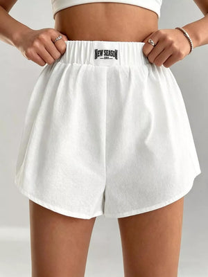 White cotton chino shorts with elastic waistband and logo tag, relaxed fit.