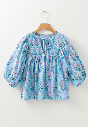 Sky blue floral print smocked yoke blouse with tie neck and puff sleeves.
