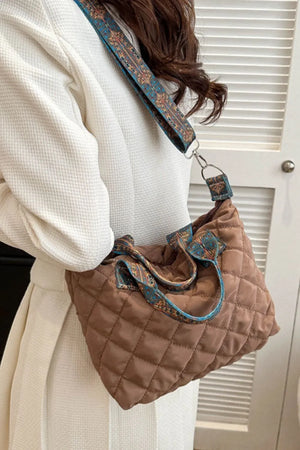 Quilted satchel bag in taupe with a colorful patterned strap and top handles.