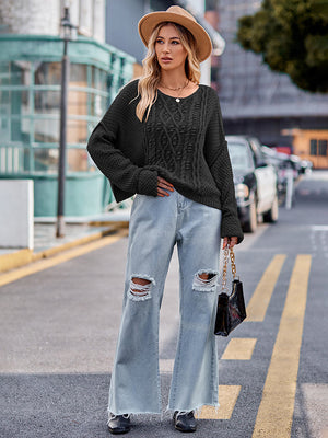 Black cable-knit sweater with a relaxed fit and crew neckline, styled with distressed jeans.
