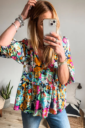 Vibrant floral print tiered blouse with tassel trim and tie neck.