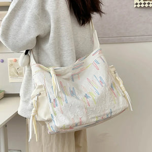 White slouchy shoulder bag with colorful embroidered lines and tassel details.