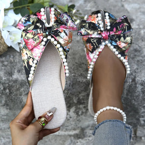 Floral bow pearl embellished slides with a black floral pattern.
