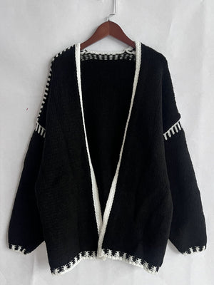 Black oversized knit cardigan with white contrast stitching detail on edges and sleeves.