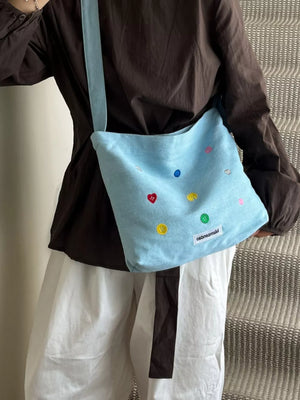 Light blue denim crossbody bag with colorful button embroidery and adjustable strap.