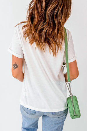 White graphic t-shirt with rolled sleeves and a round neckline, styled with jeans and a green crossbody bag.