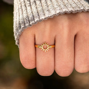 Gold sunburst signet ring on a finger, styled with a grey sweater.