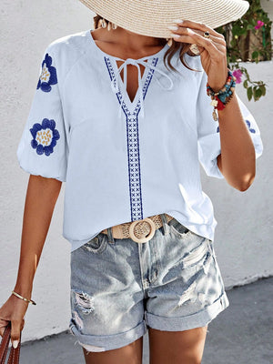 White embroidered yoke sleeve blouse with tie neck and blue floral details.