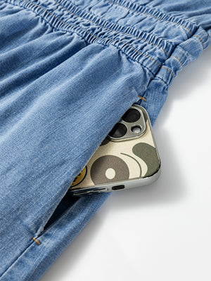 Chic denim dress with elastic waist detail and a pocket holding a phone.