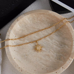 Layered gold necklace with a sparkling sun pendant.