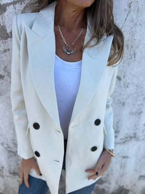 Ivory double-breasted blazer with sculpted lapels and black buttons, styled with a white tank and necklace.