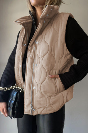 Quilted stand-collar gilet in beige with a zip and snap closure, styled with a black sweater and leather pants.