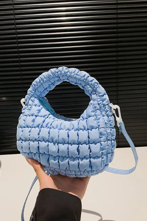 Pastel blue padded crescent crossbody bag with sculptural texture and white hardware.