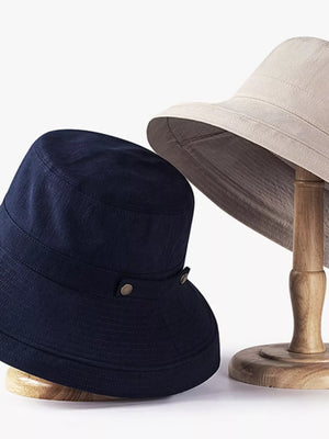 Dark navy cotton bucket hat with brass hardware detail, shown with a khaki hat.