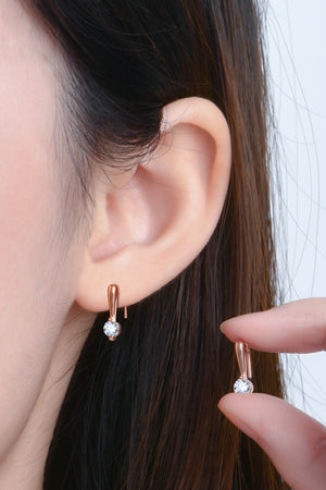 Rose gold moissanite hook earrings with a single sparkling stone, shown on ear and held by fingers.